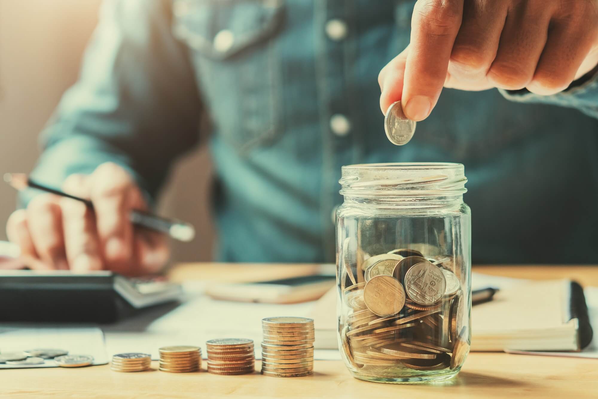 Man stacking coins and putting coins in a jar.